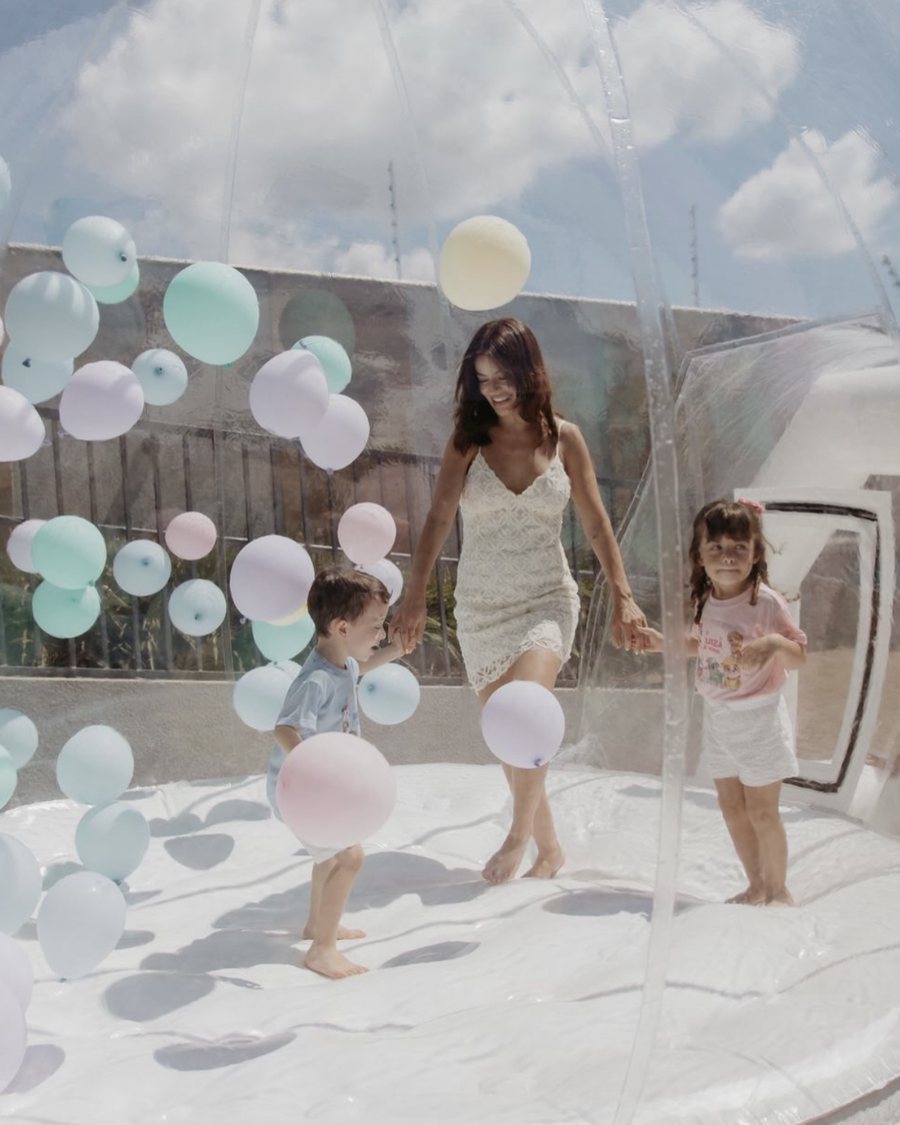 Família brincando dentro da Bubble transparente cheia de balões em tons pastel